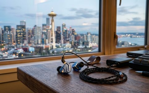 Budget IEM headphones on a wooden desk with a city view.